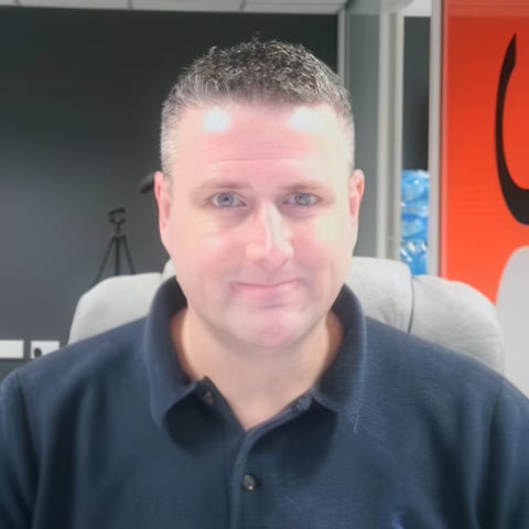 Middle-aged man with short gray hair wearing a dark blue polo shirt in an office setting