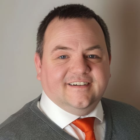 Professional headshot of a man with dark hair wearing a gray jacket, white shirt, and red tie, smiling at the camera