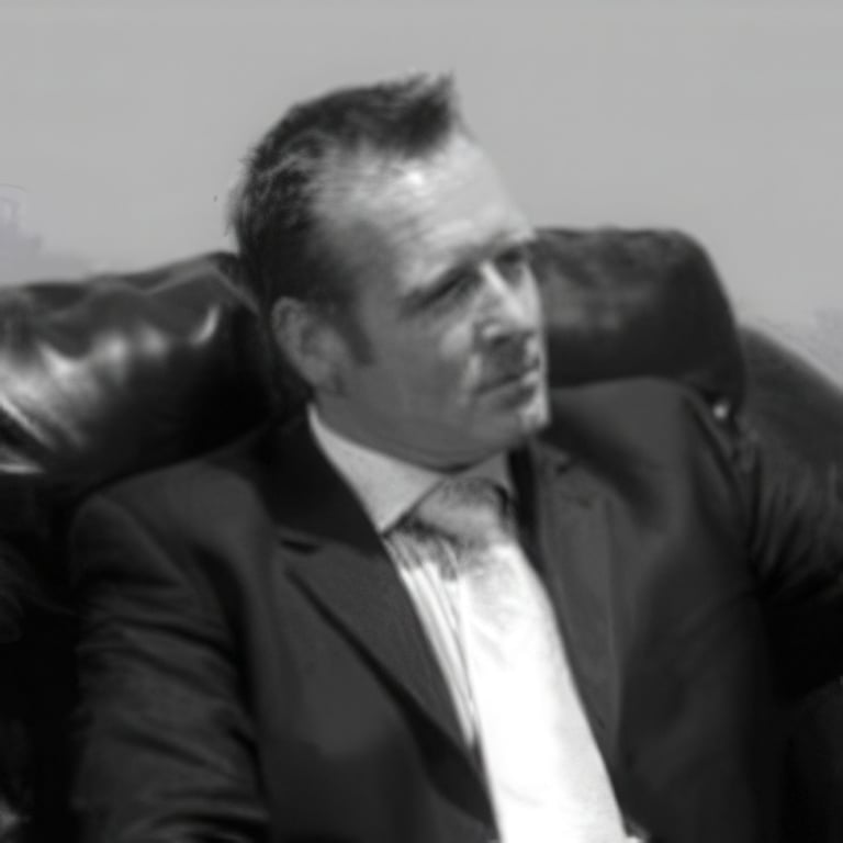 Black and white photograph of a man in a dark suit and white dress shirt, reclining on a leather chair with a contemplative expression