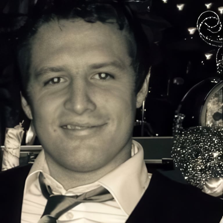 Black and white portrait of a man in formal attire with bow tie, smiling at camera with blurred festive lights in background