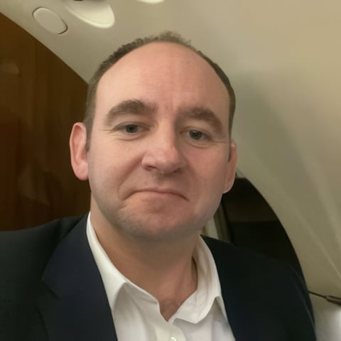 Middle-aged man with receding hairline wearing dark blazer and white dress shirt, photographed indoors
