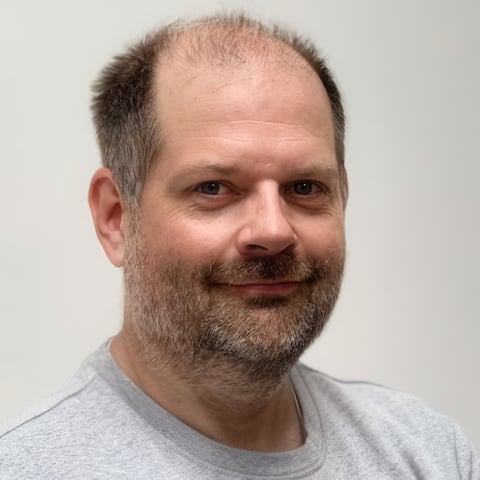 Middle-aged man with beard and receding hairline wearing a gray t-shirt, against a white background