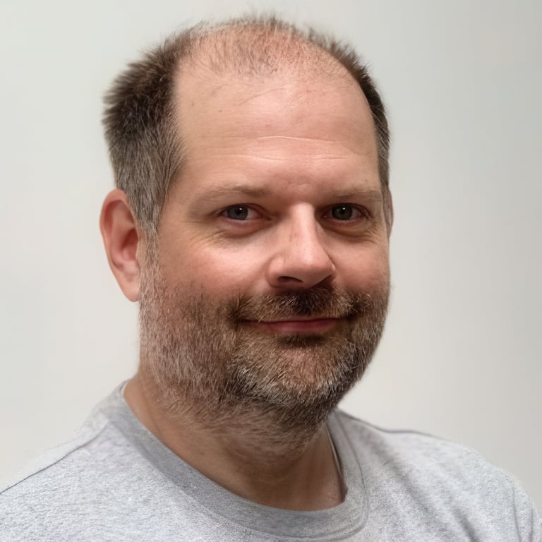 Middle-aged man with beard and receding hairline wearing a gray t-shirt, against a white background